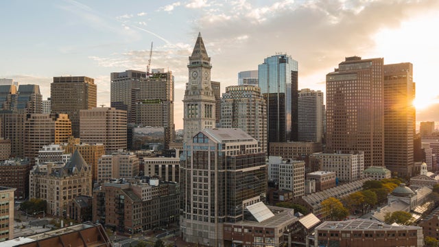 Financial district of Boston, Massachusetts. Skyscrapers skyline with famous Custom House Clock Tower and Faneuil Hall in the evening with visible sunbeam. 